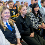 Goście konferencji, w tym młodzież - uczniowie i uczennice słuchają ze skupieniem i uśmiechem przemawiającego.